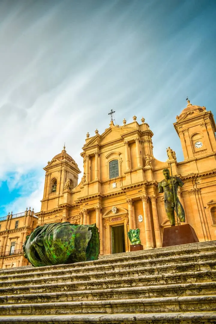 Cattedrale con sculture sulla scalinata, cielo parzialmente nuvoloso.